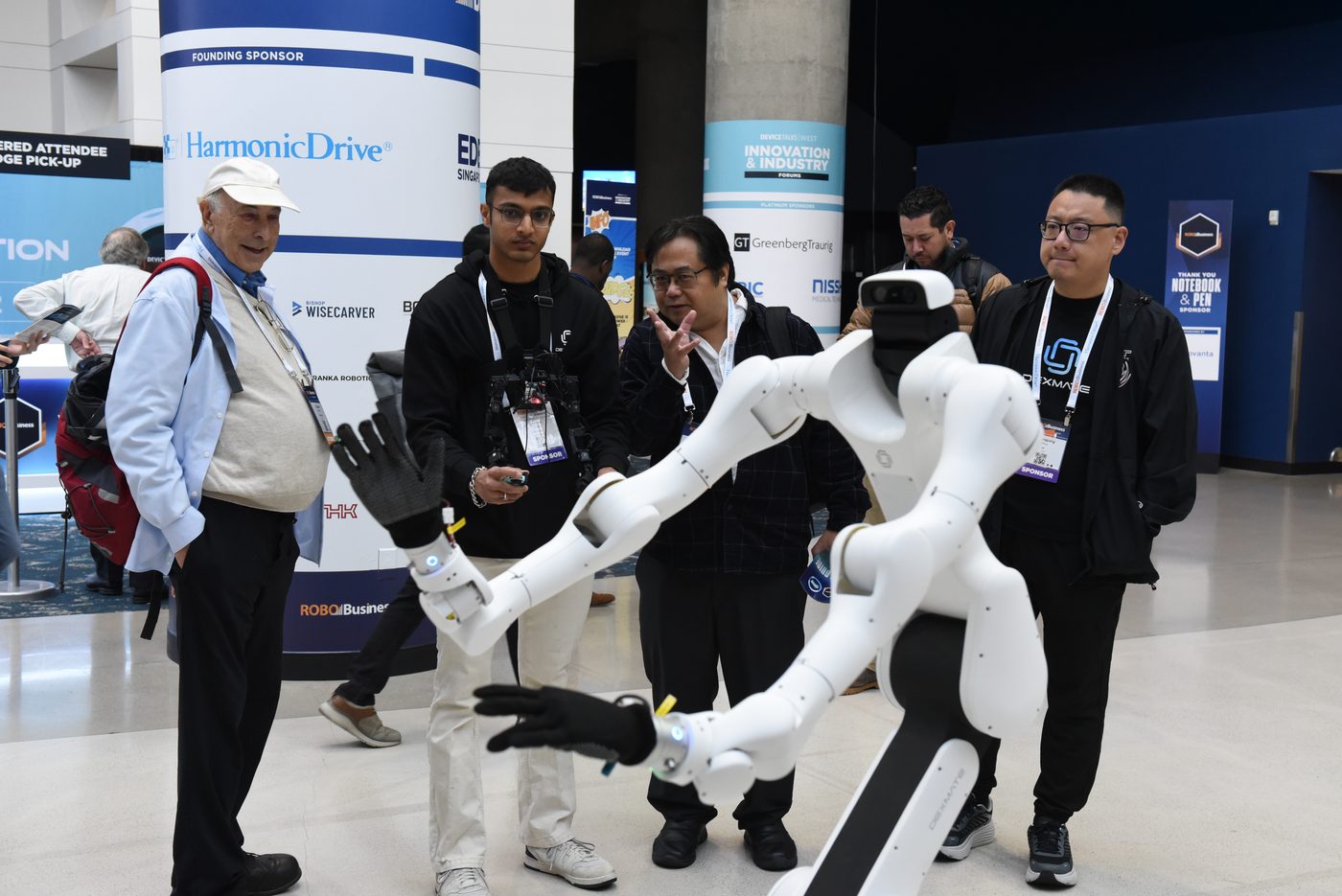 Attendees watching a white dual-arm mobile manipulator robot being demonstrated on the show floor