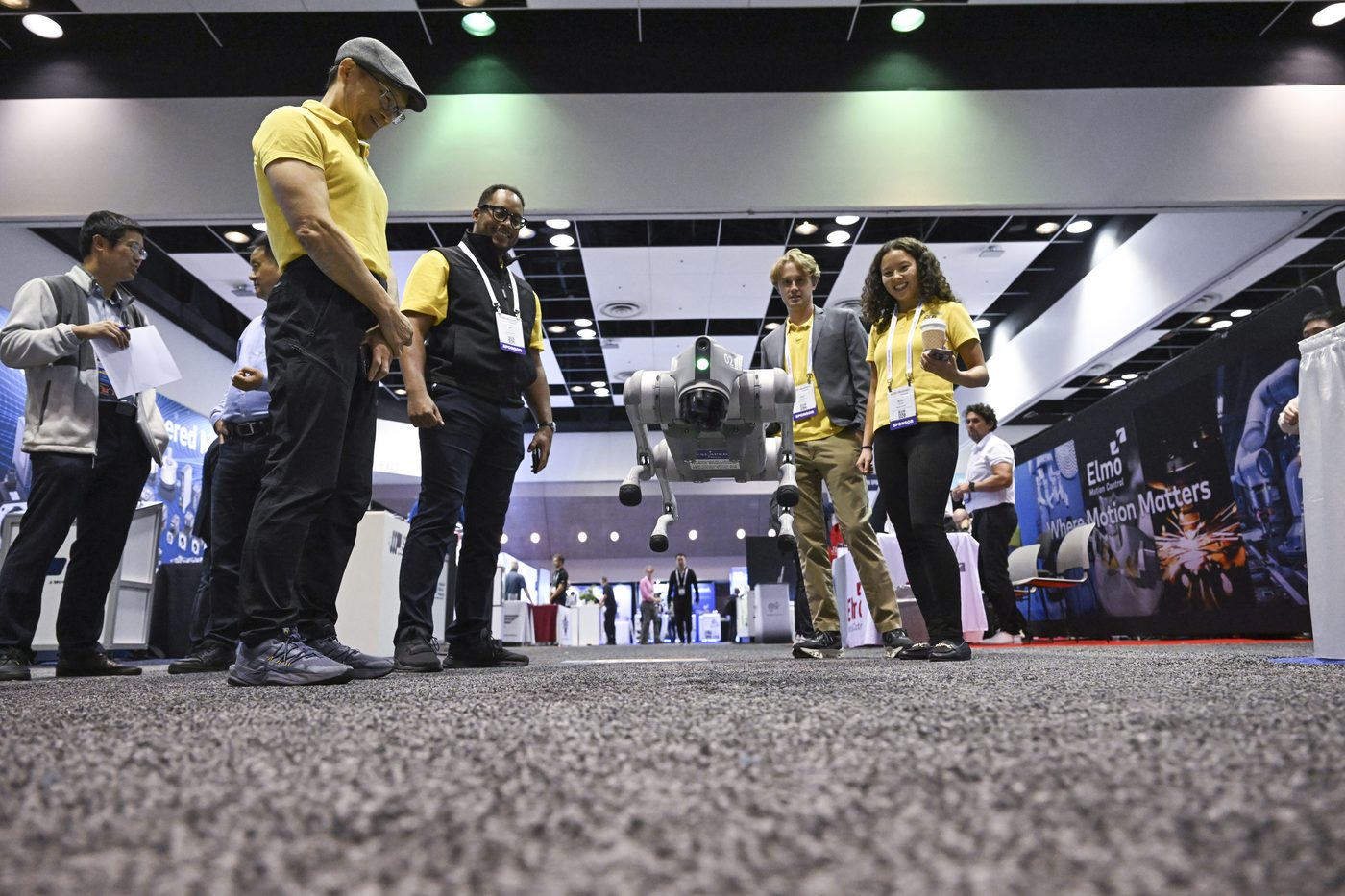 A quadruped robot dog walking across the expo floor as attendees watch